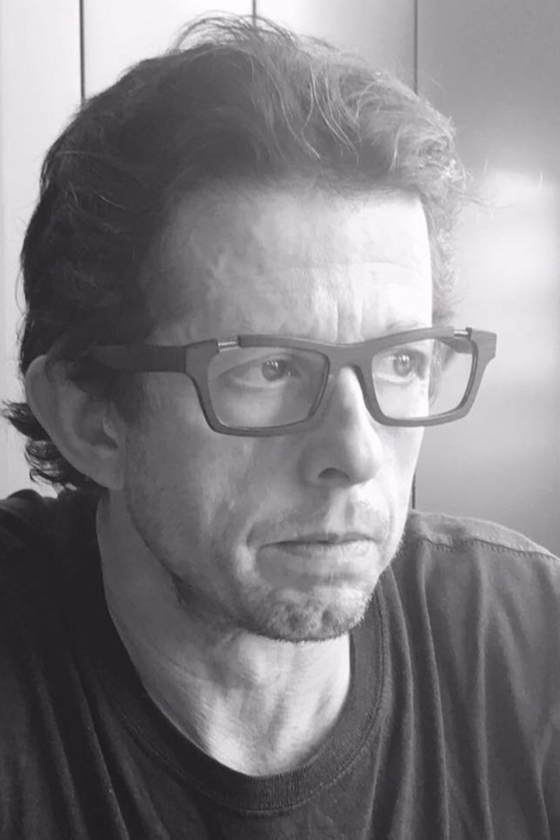Black and white portrait of a Alex Elford wearing glasses.