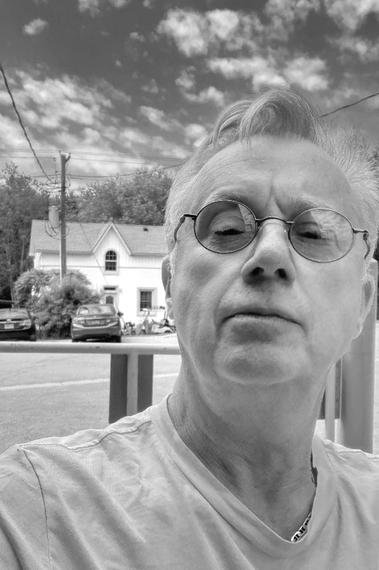 Person with glasses in front of a house and cars on a street