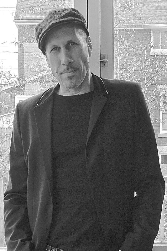 Man wearing a coat and cap standing in front of a window with a building exterior visible