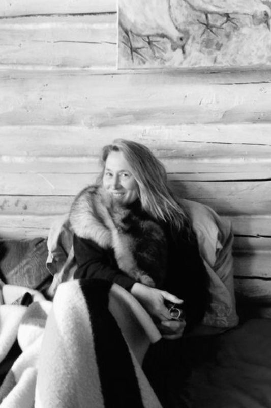 Woman sitting on a wooden bench with a fur-trimmed coat in a rustic setting.