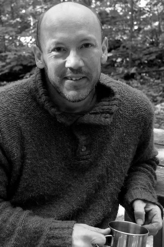 Man holding a metal cup outdoors with trees in the background