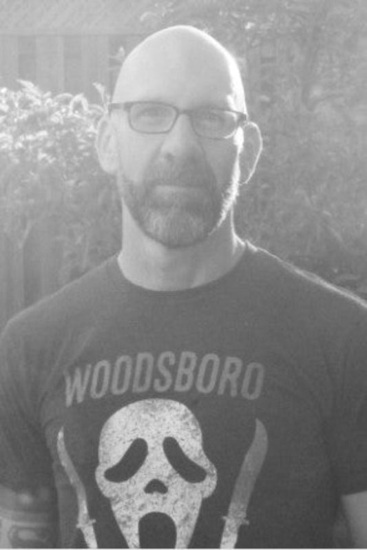 Person wearing a 'Woodsboro' t-shirt with a graphic design, standing outdoors.
