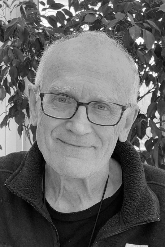 Black and white photo of a man with glasses and a jacket in front of leafy background