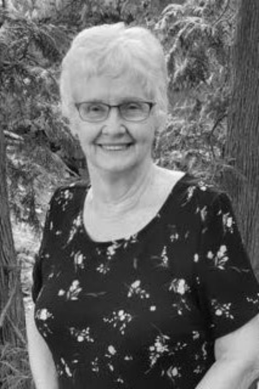 Black and white photo of a woman standing outdoors with trees in the background