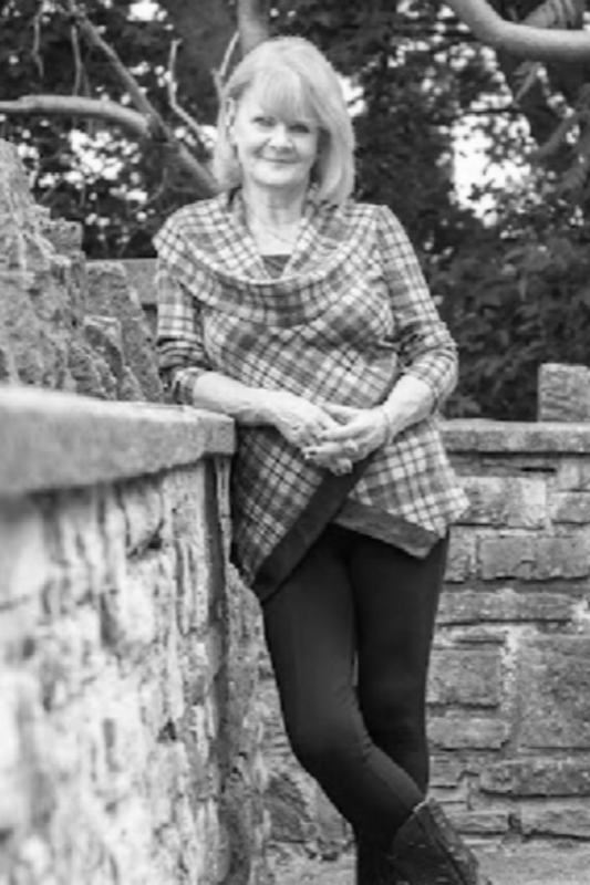 Woman wearing a plaid shirt leaning against a stone wall outdoors