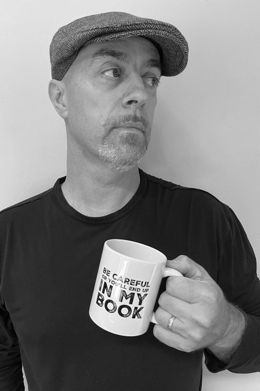 Man holding a mug with text, wearing a cap and black shirt against a white background