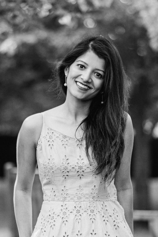 Black and white photo of a woman wearing an embroidered dress outdoors.