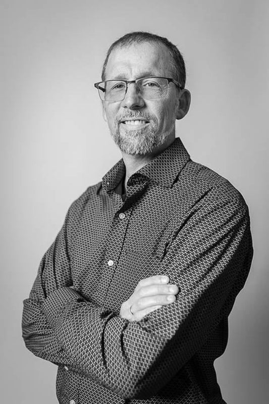 Black and white portrait of a man with glasses and a patterned shirt against a gray background