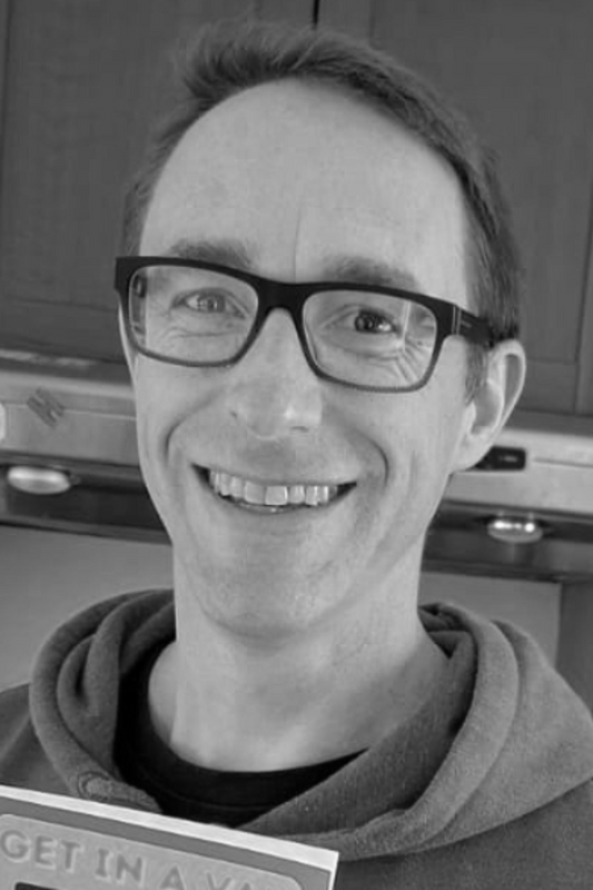 Andrew Stewart, a man with short dark hair and glasses, wearing a hoodie and holding a book.