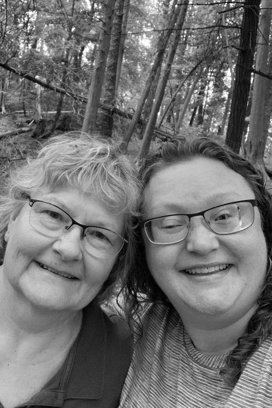 Two women with glasses standing close together in a forest setting