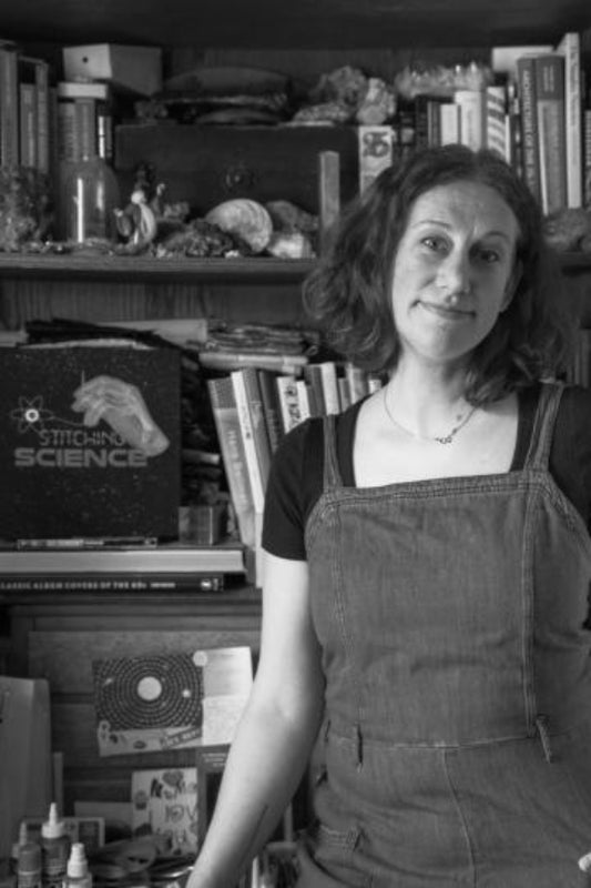 Woman wearing overalls standing in a room with books and a computer.