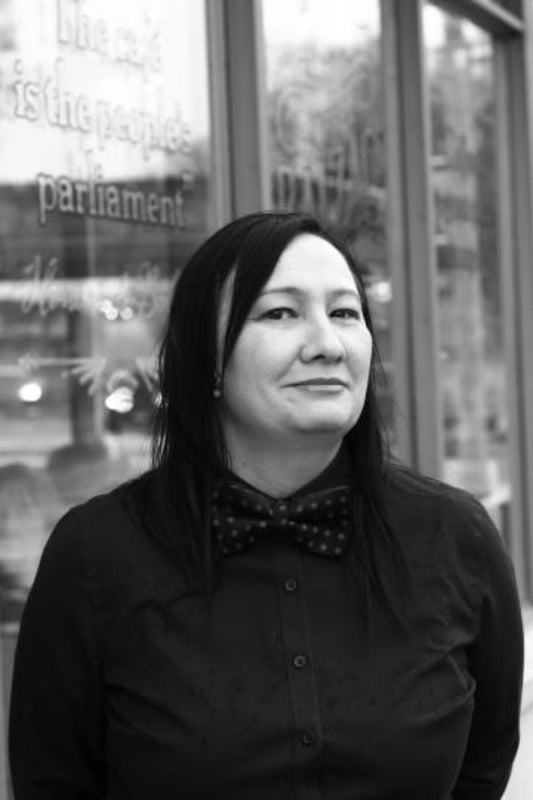 Black and white photo of a person wearing a bow tie in front of a glass door.